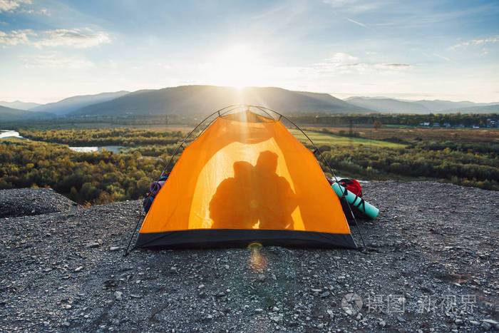 日落时分,一个年轻人和他的女朋友在山顶的橙色帐篷里亲吻对方的剪影.